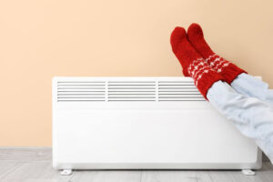 A person wearing a pair of fuzzy red socks leaning their feet against a heating system.