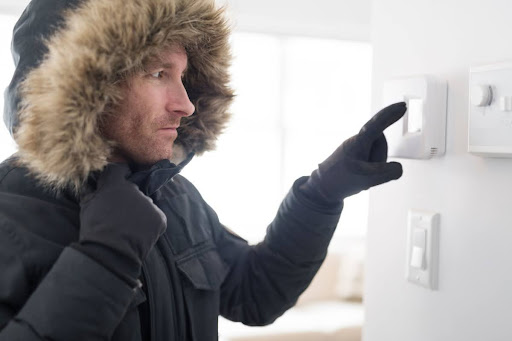 A man in a winter coat adjusting the thermostat in a home.