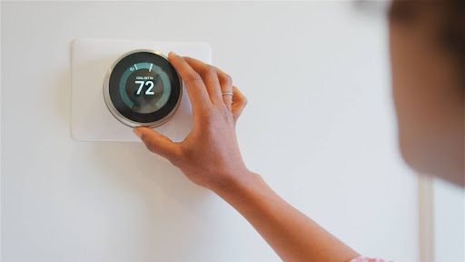 A woman adjusting a thermostat.