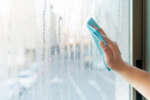 A hand using a cloth to wipe condensation off of a window.