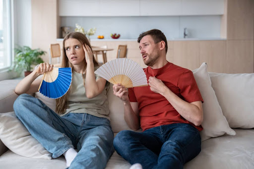 A couple fanning themselves on a couch in a hot home.