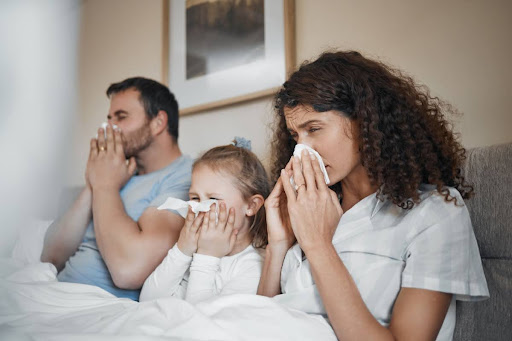 A family blowing their noses as they lay in bed.